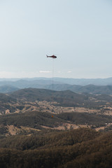 Fototapeta na wymiar Mount Comboyne - December 30th 2019: A helicopter drops water on a spot fire as seen from the top of Mount Comboyne.