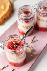 rot weißer Erdbeer Käse Sahne Kuchen im Glas mit Boden Biscuit auf rosa ovalem Teller