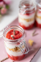 rot weißer Erdbeer Käse Sahne Kuchen im Glas mit Boden Biscuit auf rosa ovalem Teller