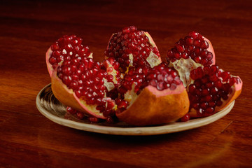 ripe juicy grains of pomegranate fruit lie on a clay plate, dark background