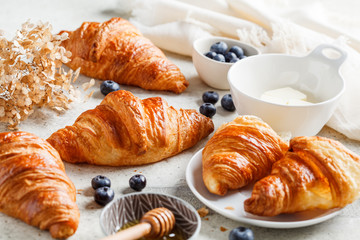 Fresh croissants with blueberries, butter and honey, gray background.