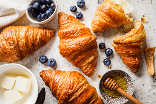 Fresh croissants with blueberries, butter and honey, gray background, top view.