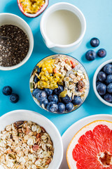 Chia pudding with blueberries, passion fruit and granola in glass, blue background. Healthy breakfast concept.