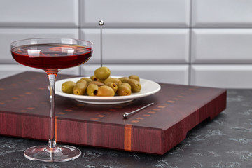 Elegant glass of red wine on a thin stem and olives on a plate standing on a cutting Board. Mediterranean snacks and tapas.