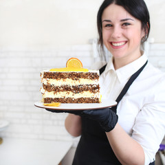 Confectioner girl holding a cutaway orange cake in her hands and smiling