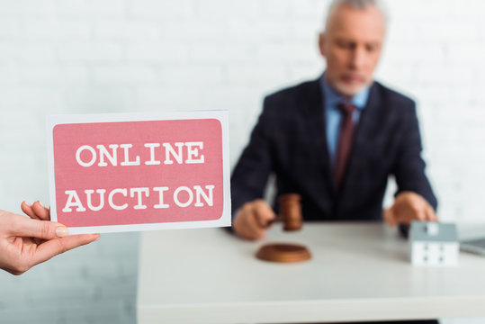 cropped view of woman holding card with online auction lettering and auctioneer holding gavel