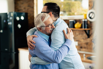 Happy senior man embracing his adult son in the kitchen.