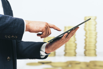 Man using digital tablet on the background of stacks of gold coins, close up. Investment concept