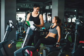 Asian man fitness trainer wearing sportswear helping and supporting his customer workout for bodybuilding in her class, Fitness gym concept
