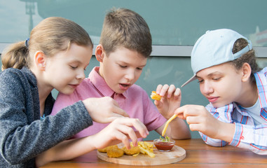 children, girls and a boy, sit at the table and eat fast food, nuggets with sauce and French fries