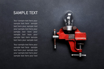 Light bulb clamped in mechanical hand vise on grey background with copy space and sample text....