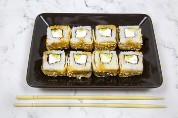 Sushi rolls with eel, avocado, cream cheese, sesame sticks in a dark plate on a light marble table, traditional Japanese food, healthy products.