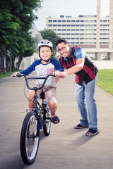 Asian man guiding his son riding a bicycle at park