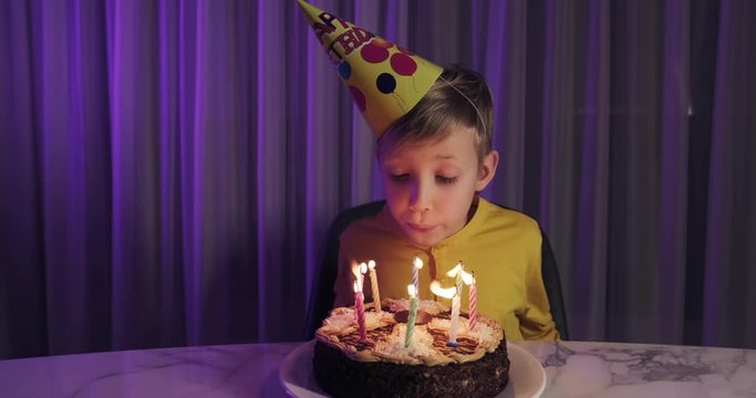 Cute boy blows out candles on a cake on his birthday.  Happy child looks at a cake with candles. Child looks at the cake and makes a birthday wish. Boy celebrates his birthday. Happiness concept