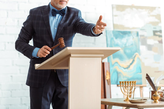 cropped view of smiling auctioneer holding wooden gavel and pointing with hand during auction