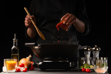 Chef adds tomato sauce to a wok with meat and vegetables.Freezing in motion. Restaurant menu,...