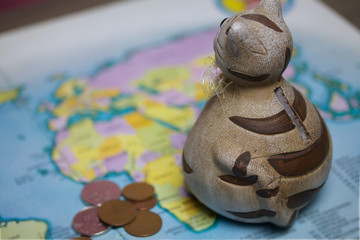 A ceramic piggy bank with a slot for coins is on the world map. Several coins are scattered nearby. Piggy bank for travel.