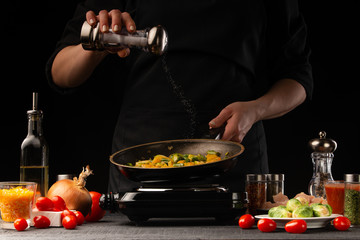 Chef fries vegetables with meat in a pan, salts. Freezing in motion. Cooking delicious food. Chef in the kitchen. Recipe book, restaurant menu.
