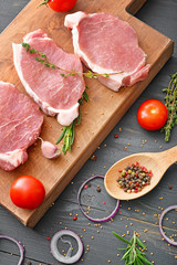 Board with raw pork meat, vegetables and spices on dark wooden background