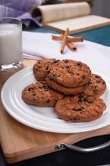 Oatmeal cookies with chocolate chips and a glass of milk on a wooden board