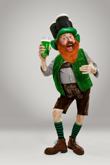 Excited leprechaun in green suit with red beard holding green beer pint on white background. Funny...