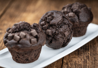 Old wooden table with fresh Chocolate Muffins (close-up shot; selective focus)