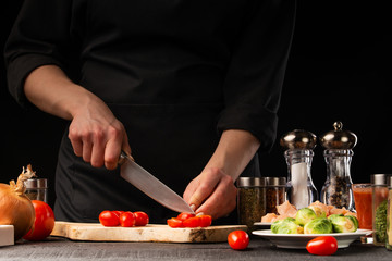 Chef cuts cherry tomatoes. Restaurant menu, cooking. On a black background, photo for advertising or design, restaurant business, cooking and recipe book.