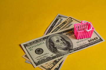 Pink shopping basket and dollar banknotes at yellow background. Shopping, personal finances, money savings concept