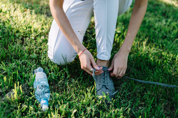 Fototapeta na wymiar Girl athlete tying shoelaces on sneakers in a summer park. Nearby is a bottle of water