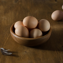 Wooden bowl with beige eggs on a wooden table.
