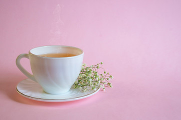 White Cup with tea on a saucer and gypsophila flowers on a pink pastel background. Good morning, Wake-up concept.Minimalistic still life. Space for copying, space for text and wording.