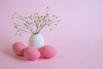 Three colorful pink Easter eggs with a bouquet of gypsophila flowers in an egg vase on a pink background. The concept of Easter holidays. Space for copying, space for text and wording. Greeting card.