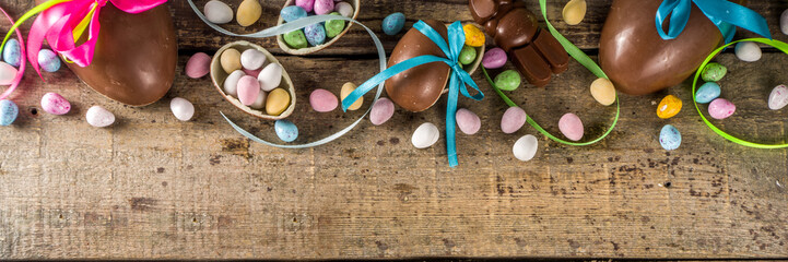 Easter card background. Chocolate Easter eggs and bunny rabbits with color ribbon and bows on wooden background