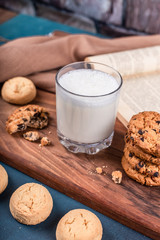 A glass of milk with sweet cookies on a wooden board.