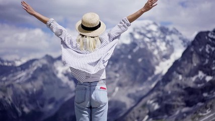 Millennial female tourist enjoying freedom in mountains Park while raising hands spread wide open with joy. Back view of young woman enjoying summer wind and nature freedom during travel. Slow motion