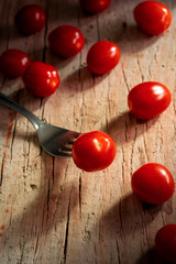 Fototapeta na wymiar Scattered fresh cherry tomatoes on rustic wooden table. One cherry tomato on tip of fork.