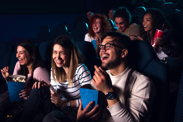 Group of cheerful people laughing while watching movie in cinema. - obrazy, fototapety, plakaty