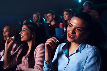 Group of cheerful people laughing while watching movie in cinema.