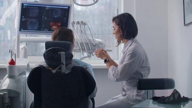 A female orthodontist dentist talks to a patient and shows problematic teeth on a cast discussing a treatment plan