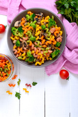 Cavatappi colored pasta with broccoli and mushrooms on a white wooden background. Pasta colorata. Pasta with vegetables. The top view