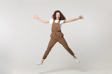 Excited young woman jumping with raised hands and straight legs.