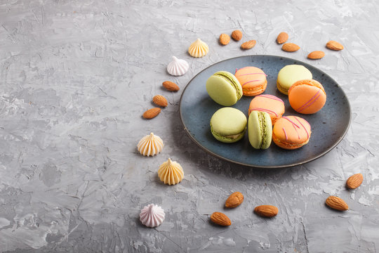 Orange and green macarons or macaroons cakes on blue ceramic plate on a gray concrete background. side view.