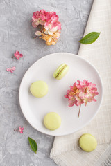 Fototapeta na wymiar Green macarons or macaroons cakes on white ceramic plate on a gray concrete background top view.
