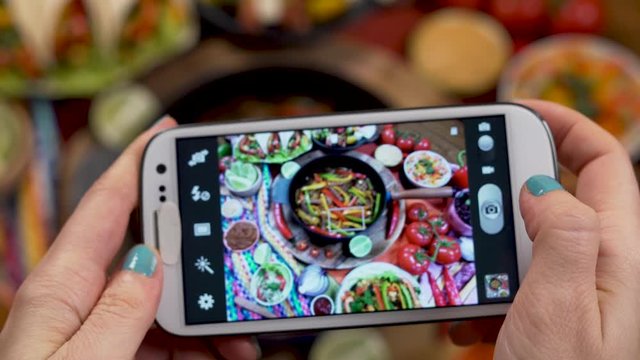 A Woman's Hands Take Photos Of Traditional Mexican Food with a Smartphone Hot Fajitas is Served with Sauces and Tortilla and Vegetables, Burritos, Bean Soup.
