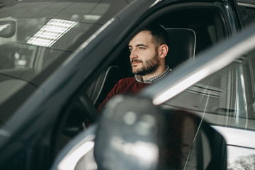 Bearded white brunette man sitting behind the wheel in a black car