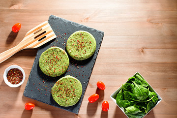 Raw green chicken and spinach burgers with spices on a stone plate in hard light, top view. Eating healthy concept, dinner idea for dieting, weight-loss-friendly foods, rustic style