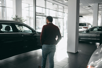 A white bearded brunette man walks in a car shop, salon, chooses a car to buy