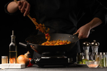 Cooking by the chef cook says Italian pasta with meat and vegetables, stirs, freezing in motion, on a black background.horizontal frame, restaurant business