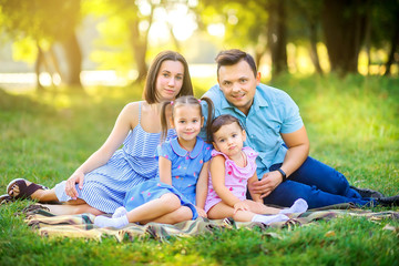 Fototapeta premium Happy family. The family walks in a beautiful park at sunset, sitting on the grass and smiling, family time.