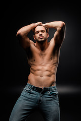 Fototapeta na wymiar handsome and muscular man in jeans touching hair on black